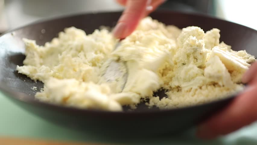 Close-up of female hands mixing fresh cottage cheese in a bowl with a spoon. Rustic homemade dairy preparation in a cozy kitchen with organic ingredients