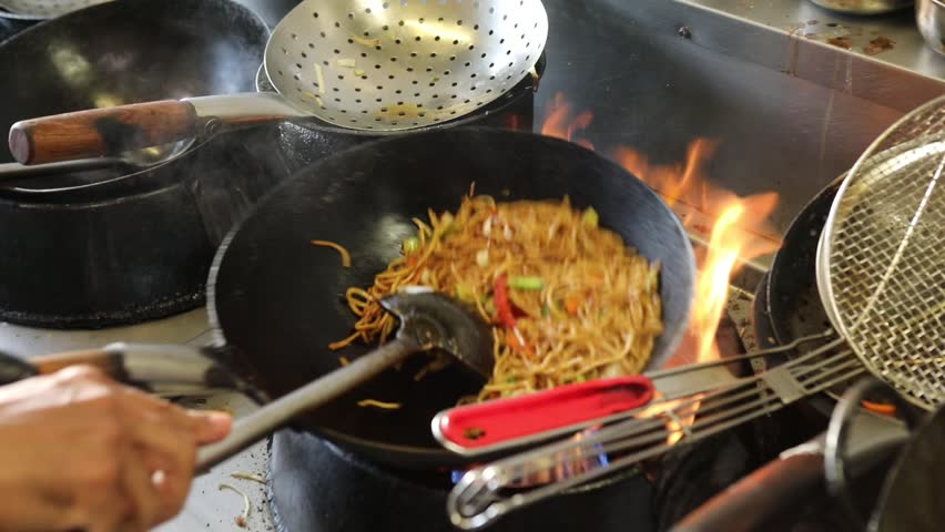Professional chef cooking Asian noodles with vegetables in a hot wok pan at a bistro kitchen. Perfect footage for themes of street food, gastronomy, Asian cuisine, and culinary arts.
