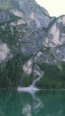 Vertical screen of Lago di Braies with rocky cliff and pine trees reflecting in water