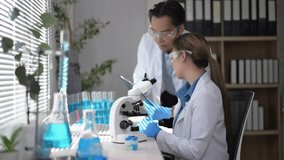 Two scientists are working together in a lab, one of them is wearing a lab coat and the other is wearing a white lab coat. They are both wearing safety goggles and are looking at a microscope - Powered by Shutterstock - Get 15% off with code: PIKWIZARD15