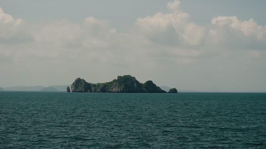 A rugged rocky island with green vegetation rises from the sea near Ko Tao, Thailand.