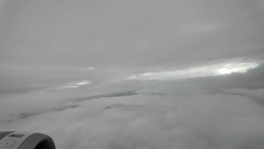 A plane is flying through a cloudy sky. The clouds are white and grey, and the sky is mostly overcast. The plane is low to the ground, and the clouds are close to the plane