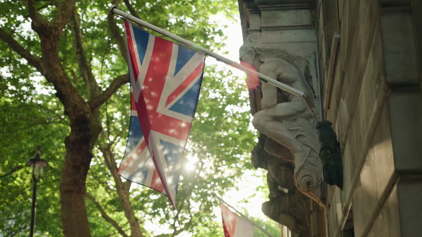 Union Jack flag hanging on a historic building with green trees on the background in London, England