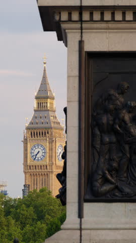 Close-up view of the Big Ben clock tower illuminated by golden sunlight, partly framed by a historic monument in London, England. Vertical