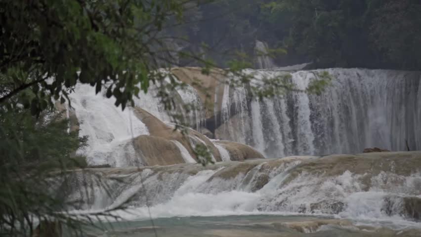 The tiered Agua Azul Waterfalls in Chiapas, México, highlighting the rapid descent of water over light-colored, rocky ledges and the surrounding jungle foliage.