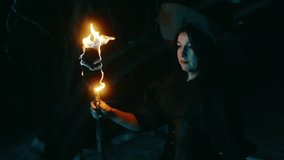 Mysterious woman in black witch hat walks with torch flame in forest at night with smoke, symbol of Halloween mysticism and ritual. - Powered by Shutterstock - Get 15% off with code: PIKWIZARD15