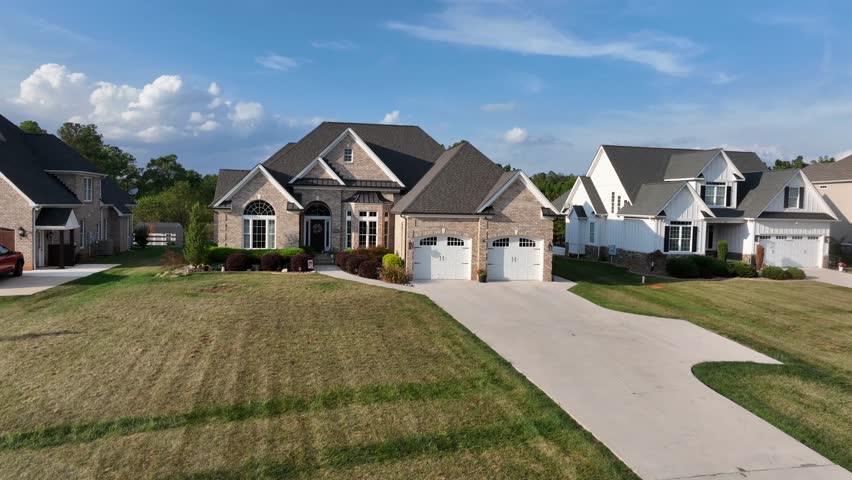 Aerial approaching short of modern american suburban style house with double garage and grass in front yard. Sunny summer day in Virginia, USA. Brick house and multiple gables.