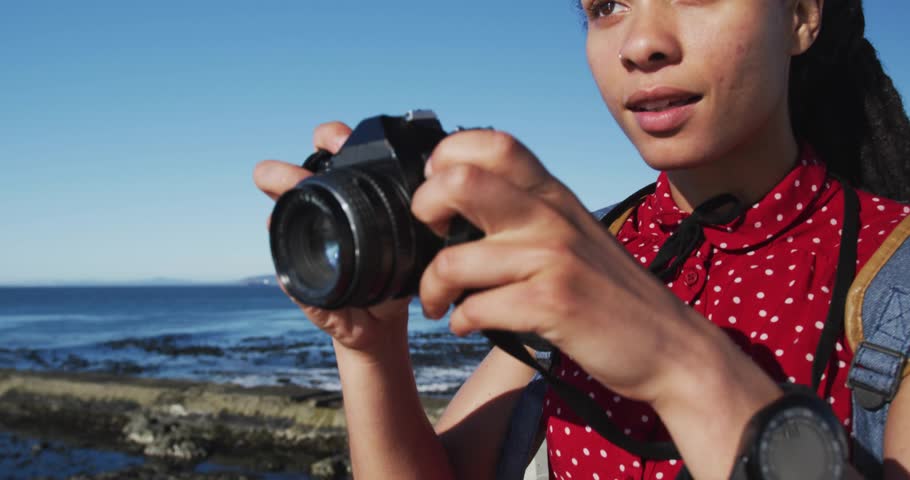 Woman using camera on shore, focusing lens initiating purple-blue swirl wrapping gear for tech demo. Adventure, exploration, innovation, digital art, vibrant, nature, creativity