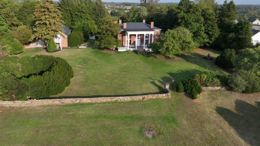 Aerial flyover house with red brick and four chimneys in rural district of American town. Sunny autumnal day in USA. Large garden and property in suburbia. Peaceful summer scene.