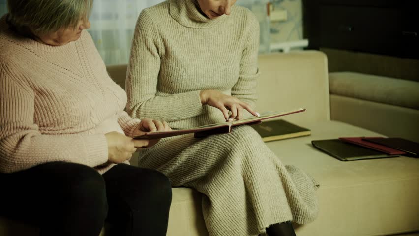 Two Women Looking At Old Photo Album. Generational Family Memories, Nostalgic Moments And History, Sharing Past Stories. Senior Mother And Adult Daughter Bonding. Memory Lane Discussion Family History