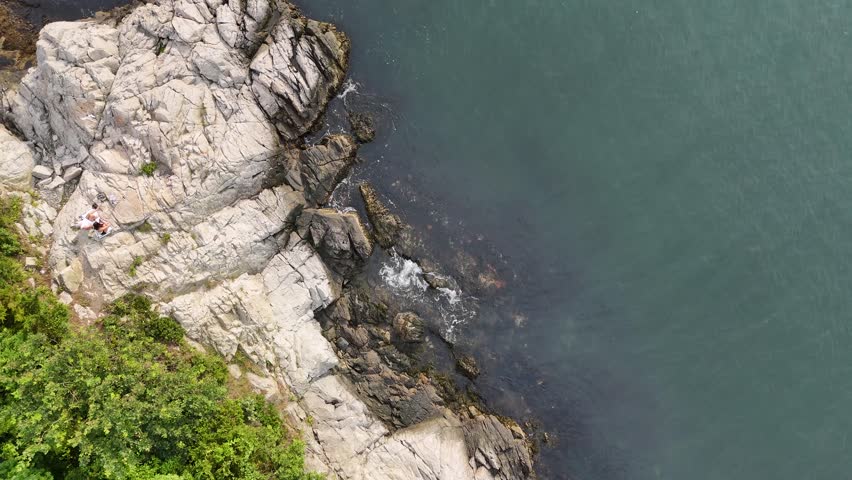 Aerial view of rocky coastline meeting lush green trees and turquoise waters, creating a striking contrast of textures and tones, Jamestown, Rhode Island, United States.