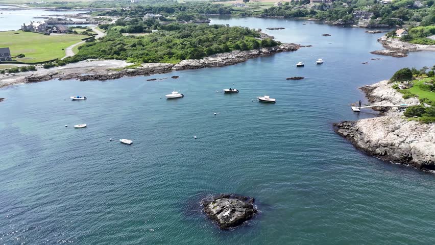 Aerial view of boats in the dark blue water near the rocky coastline and lush green trees along Ocean Avenue, Newport, Rhode Island, United States.