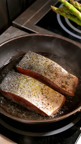 Chef adding asparagus to salmon pan. Hand adding fresh asparagus while salmon fillets are frying in a pan.