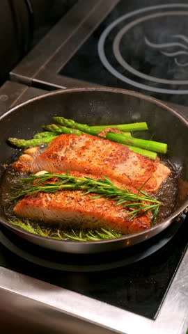 Salmon fillets with asparagus and rosemary in pan. Two pieces of salmon are fried in a pan with asparagus and rosemary branches.
