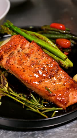Grilled salmon fillet with asparagus and rosemary on black plate. Close up of roasted salmon served with asparagus, rosemary and sauce on a gourmet plate.
