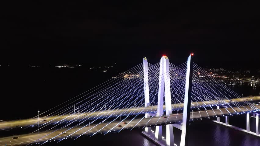 Aerial view of the illuminated Governor Mario M. Cuomo Bridge spanning the dark waters, reflecting the bridge