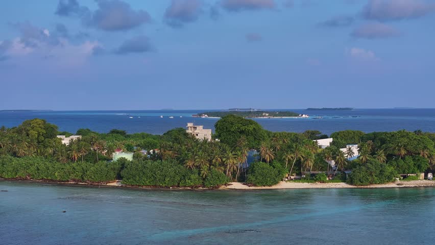 Aerial view of an island with lush green trees, white buildings, and turquoise water, creating a tropical paradise, Kamadhoo, Baa Atoll, Maldives.