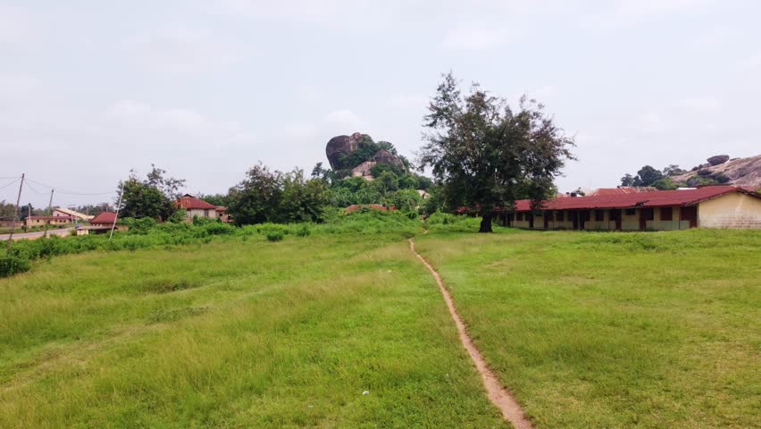 Aerial view of a landscape with dominant rock formations, lush greenery, and scattered buildings, creating a vivid contrast in Akure, Ondo, Nigeria.