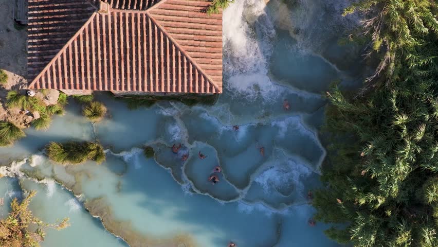 Aerial view of tiered thermal springs with bathers enjoying the milky blue water and creamy white stone formations, Saturnia, Toscana, Italy.