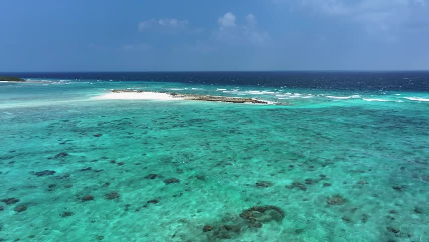 Aerial view of the vivid turquoise ocean contrasting against the dark blue sea, with a small island in the shot, Naavaidhoo, Haa Dhaalu Atoll, Maldives.
