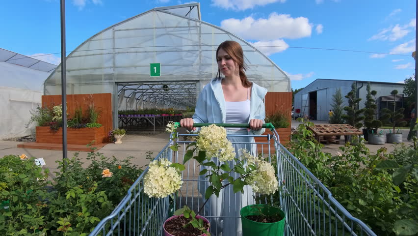Woman with shopping cart full of flowers outside greenhouse