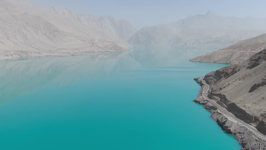 Aerial view of the turquoise Baisha Lake contrasting with the muted tones of the surrounding mountains and road, Baisha Lake, Xinjiang, China.