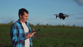 Man controlling drone with tablet over green field while quadcopter hovers near pilot showing remote control operation for agriculture survey and flying inspection in open landscape equipment - Powered by Shutterstock - Get 15% off with code: PIKWIZARD15
