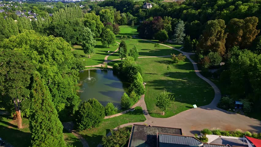 Parc des Ondines, Changé, France, lake with fountain, green lawns, and lush trees on sunny day. Aerial forward