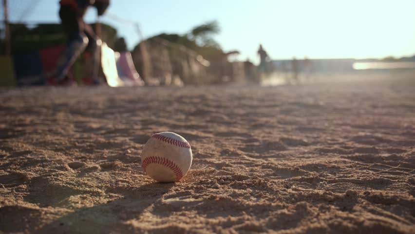 Baseball player running and sliding into a base on a dusty field during a game at sunset