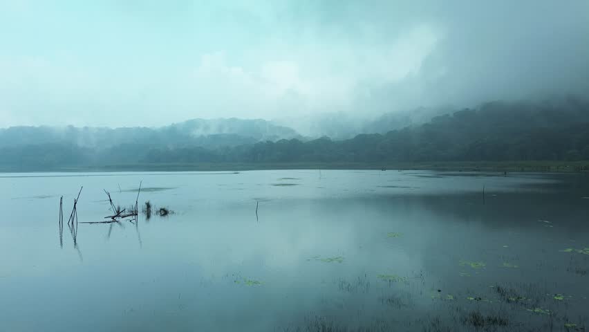 Aerial view of a lake in the mountains at dusk, fog all around. Mystical atmosphere. Wooden boats of fishermen are nearby, but there are no people. Trees and forest near the water.