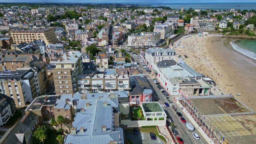 Aerial of Plage de l’Ecluse in Dinard with beachgoers, turquoise water, and promenade, summer establishing