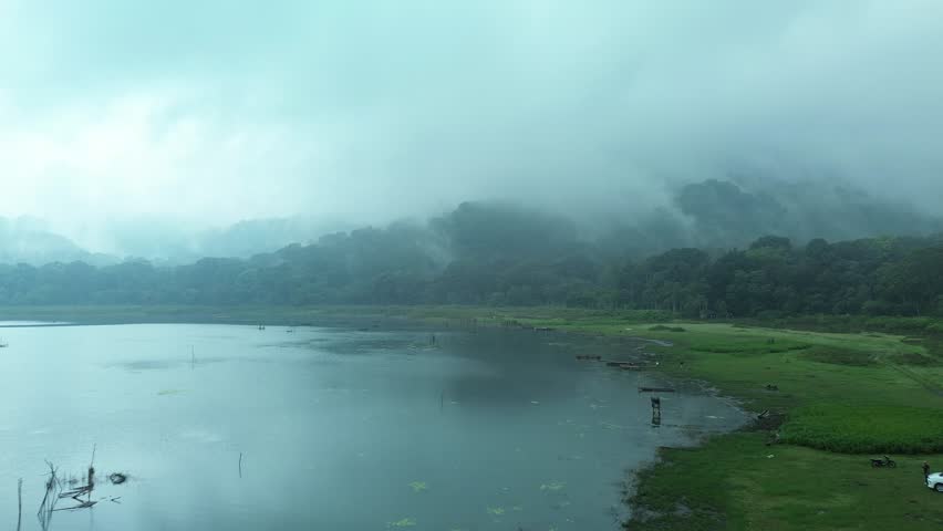 Aerial view of a lake in the mountains at dusk, fog all around. Mystical atmosphere. Wooden boats of fishermen are nearby, but there are no people. Trees and forest near the water.