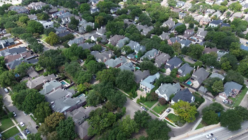 Upscale narrow-lot two-story homes in Highland Park, Dallas, private swimming pools, mature trees, compact backyards, proximity to busy US 75 highway, blending suburban comfort with urban access. USA