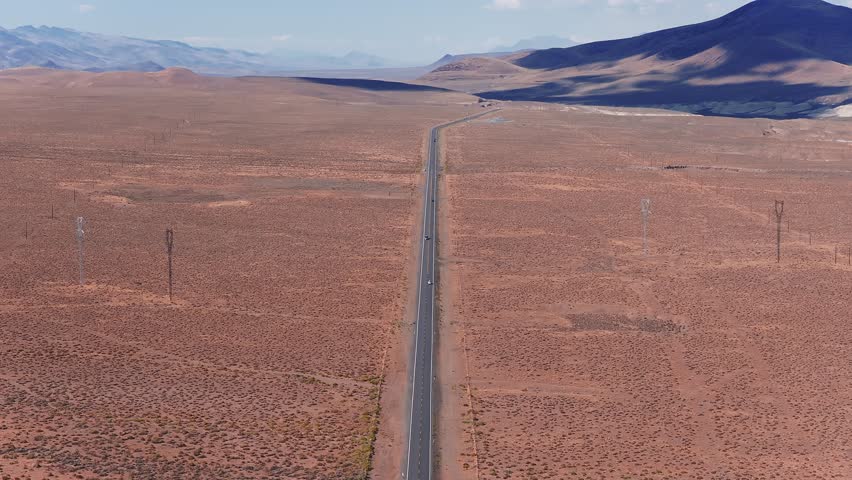 A slow aerial pan over Nevada's desert landscape, featuring a straight road, sparse vegetation, distant mountains, and a solar panel field.