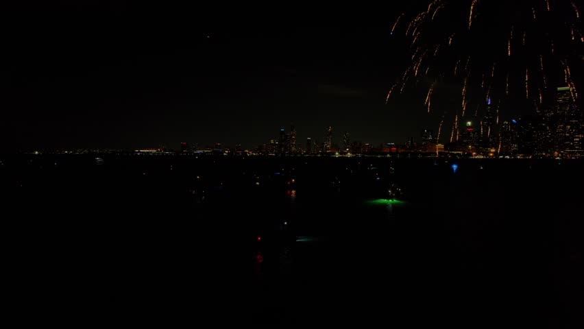 Bursts of holiday fireworks over the urban Chicago downtown city skyline and the dark reflective waters.
