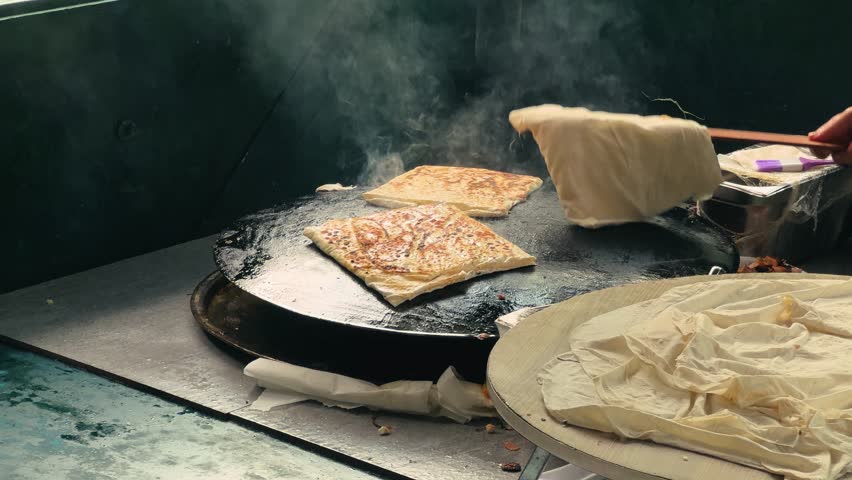 A woman preparing unleavened bread for Gözleme, a savory Turkish pancake, cooked on a wide, round griddle.