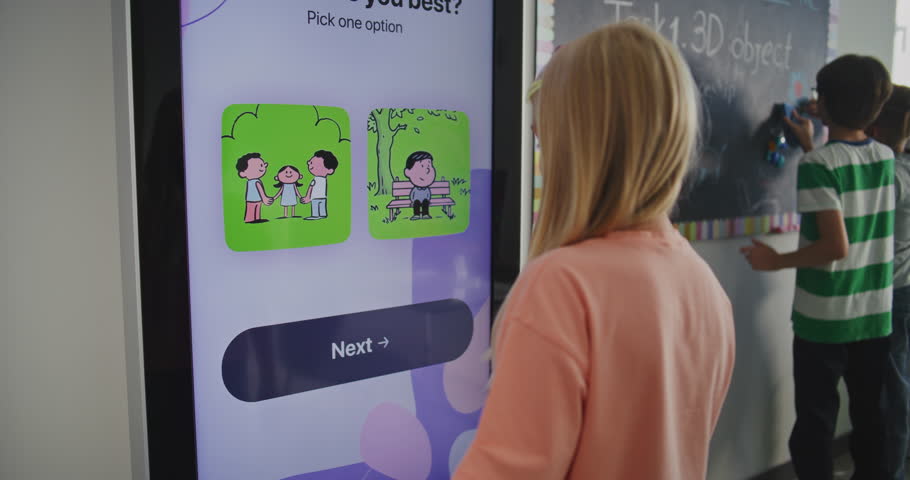 Young Blonde Schoolgirl in Classroom Takes Temperament Test on Digital Screen. Other Students Write on Blackboard. Concept of Emotional Intelligence, EdTech, and Student Well Being. Back View.