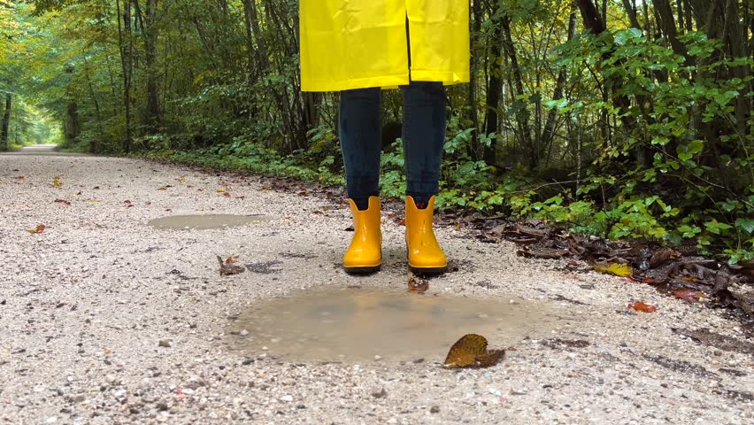 yellow rubber boots in the rain, legs in jeans and boots jumping in a puddle during rain, splashes of water in autumn park	