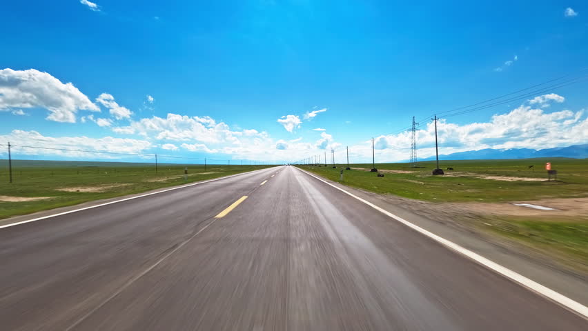 A fast car driving on an empty asphalt highway through vast green grasslands under blue sky