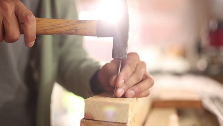 A man is hammering a nail into a piece of wood