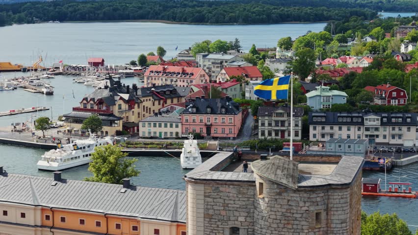 Vaxholm fortress and Vaxholm city, Stockholm County, Sweden, Stockholm archipelago. Swedish flag flying proudly on the tower of historic stone Vaxholm Fortress.