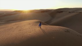 Lonely woman in a blue robe walking along a sand dune crest during a scenic desert sunset in Morocco - Powered by Shutterstock - Get 15% off with code: PIKWIZARD15