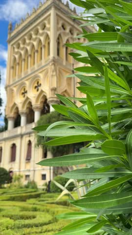 Cinematic view of historic villa on Isola del Garda, Italy. Venetian neo-Gothic crenellated tower, ornate architectural details, terrace, and meticulously landscaped garden