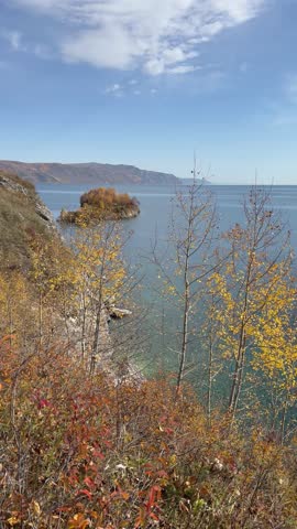 Vertical video of autumn landscape of Baikal Lake. View from rocky shore with yellow birch and aspen trees to Cape Shamansky - natural landmark on September sunny day. Nature park. Outdoor recreation 