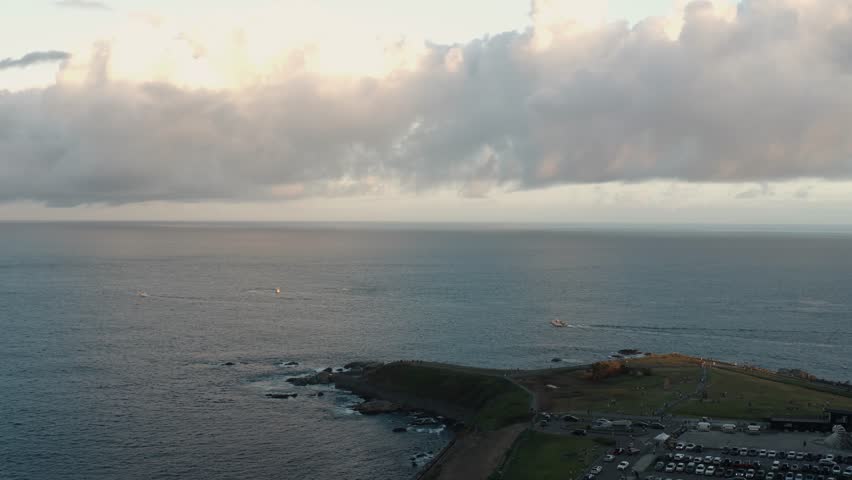 4K Aerial drone footage flying forward over green fields toward the ocean horizon. A fishing boat moves across the water and part of the coastline landscape appears in view.