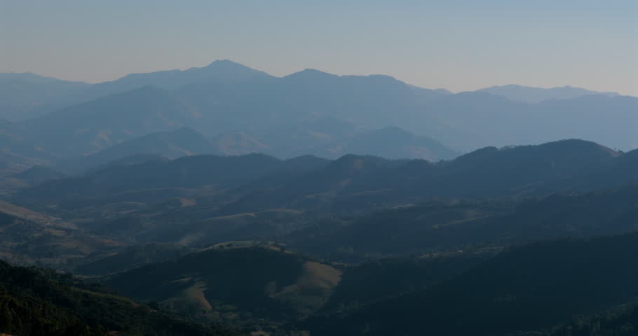 Blue mountain ridges stretching across the horizon under hazy afternoon light, layers of forested hills creating soft gradient in natural landscape