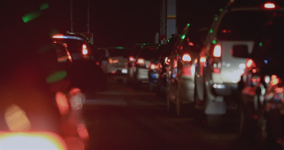 Traffic jam at night with long rows of cars and brake lights glowing red, green signal reflections and dense congestion on urban road in darkness