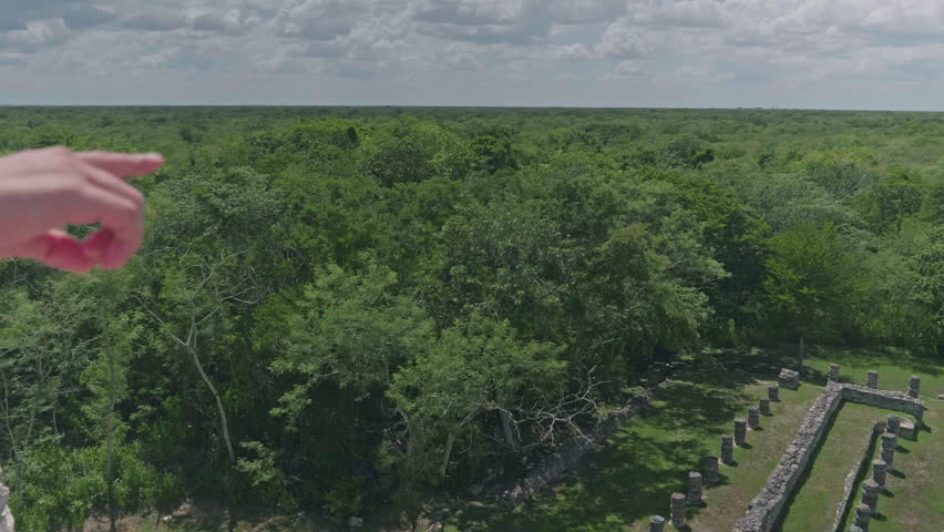 Person points overlooking dense jungle canopy from top of Mayapan pyramid, elevated shot, establishing pan