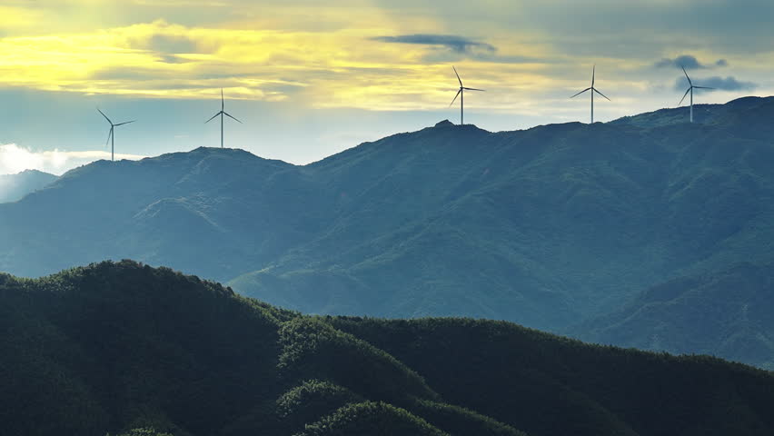 Wind turbines generating clean renewable energy on the beautiful green mountain at sunrise