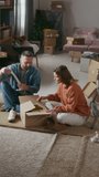 Vertical shot of man and woman unpacking cardboard boxes with their belongings while their little son trying to have fun during their relocation to new home - Powered by Shutterstock - Get 15% off with code: PIKWIZARD15